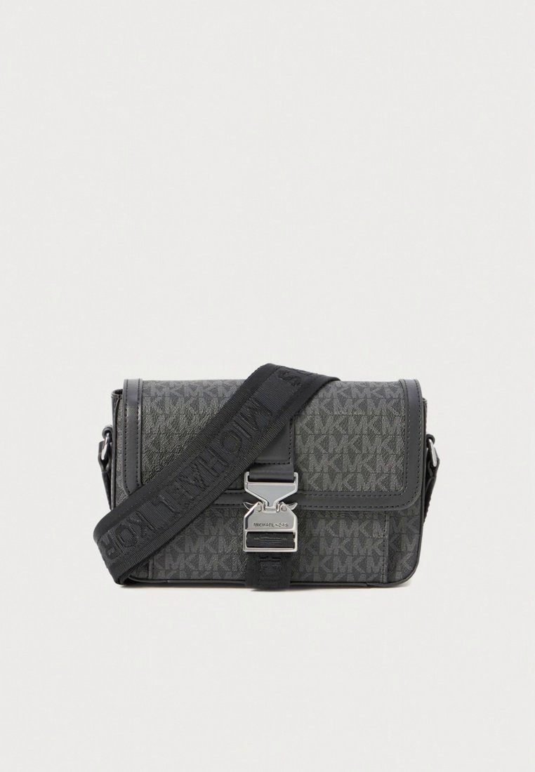 Sac bandoulière en matériau texturé noir. Présente un motif monogramme signature, une quincaillerie argentée, et une sangle ajustable avec détails logo.