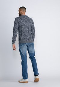 Grijze en blauwe gemarmerde gebreide trui met een ronde hals, gecombineerd met lichtblauwe spijkerbroek en witte sneakers met tankleurige zolen.