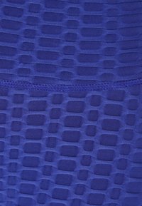 Modrá texturovaná tkanina s geometrickým vzorem vystouplých obdélníkových tvarů. Hladký a elastický materiál s jemnými detaily šití.