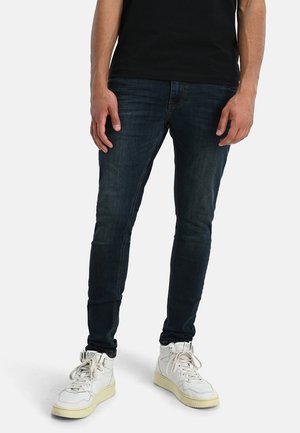 Slim-fit donkerdenim jeans, met een zachte textuur, een lichte vervaging en een klassiek vijf-pocket ontwerp, gecombineerd met witte hoge sneakers.