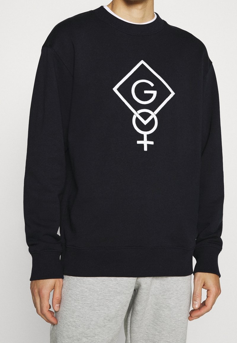 Sudadera negra con un diseño de logo geométrico blanco que presenta la letra "G" y un símbolo femenino. Material de algodón; puños y dobladillo acanalados.