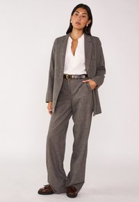 Abito grigio a righe con pantaloni a gamba larga, un blazer sartoriale e una camicia bianca con colletto. Cintura marrone e mocassini come accessori distintivi.
