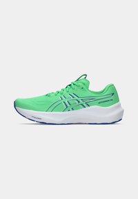 Zapatilla de running verde con un upper texturizado, que presenta acentos azules y suela blanca. Incluye cierre con cordones y un diseño de marca prominente.