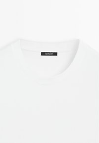 White cotton t-shirt with a round neck. Features a smooth texture and a label in black with "Massimo Dutti" and "Made in Portugal."