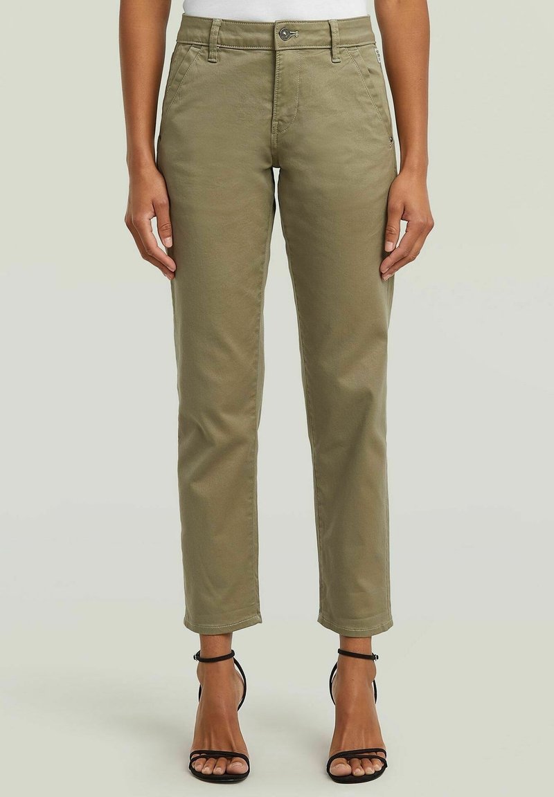 Chinos kaki avec un design à jambes droites, dotés d'une fermeture à bouton, de poches avant et d'une texture lisse. Portés avec des escarpins noirs à lanières.
