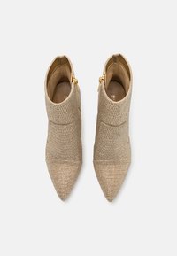 Paire de bottines beiges texturées à bouts pointus avec des fermetures éclair latérales dorées, vue de dessus sur fond blanc.