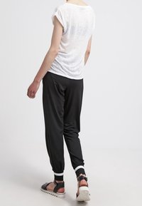 Svarta joggers med vita manschetter, lättviktig vit topp och svarta sandaler. Toppen har uppvikta ärmar; tyget verkar genomskinligt och mjukt.