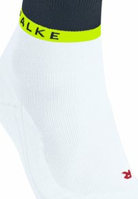 Calzino bianco alla caviglia con un bordo grigio scuro e una luminosa banda gialla che riporta il nome del marchio "FALKE" e un piccolo logo rosso sul lato.