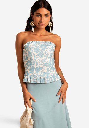 Strapless top in wit met een blauw bloemenpatroon, met een gefronst zoom. Gecombineerd met een lichtblauwe rok en een crèmekleurige stoffen tas.