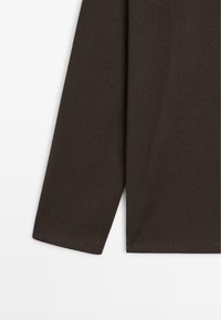 Langärmliges, dunkelbraunes Hemd, das den Ärmel und die untere Seite vor einem weißen Hintergrund zeigt.