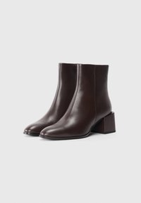 Bottines en cuir marron avec une finition lisse, bout pointu et talon bloc géométrique. Design épuré avec une silhouette simple.