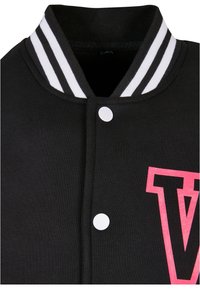 Svart varsity-jakke med hvit stripete krage, hvit trykknapplukking og et fremtredende rosa bokstav "V" på forsiden.