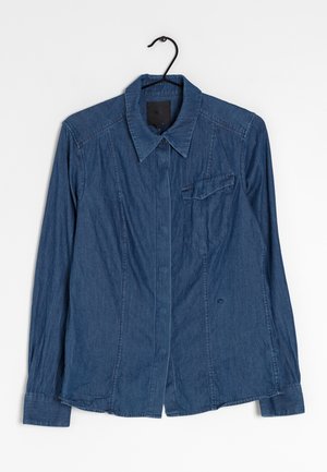 Camicia di jeans blu scuro, con collo appuntito, maniche lunghe, tasca frontale e dettagli cuciti. Taglio dritto.