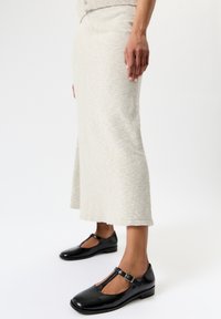 Vaaleanharmaa neulottu hame, jossa on liehuva helma, yhdistettynä mustiin kiiltäviin Mary Jane -kenkiin, joissa on T-nauha ja solkikuvio.