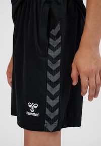 Pantaloncini sportivi neri realizzati in materiale leggero, con un motivo a chevron spesso bianco e nero lungo il lato e un logo bianco.