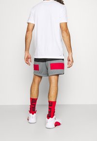 Valkoinen t-paita, harmaat shortsit mustilla ja punaisilla paneeliakselilla, punaiset sukat ja valkoiset kengät punaisilla yksityiskohdilla. Yksinkertainen urheiluvaatetus takaa.