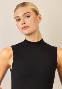 Top senza maniche nero con scollatura alta, realizzato in un morbido tessuto a maglia. Texture liscia e design aderente, che mette in risalto una silhouette pulita.