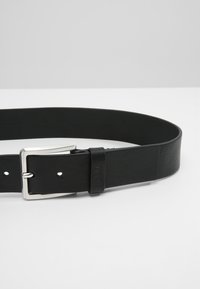 Cintura in pelle nera con finitura liscia, dotata di una fibbia in metallo argentato e fori regolabili per una vestibilità sicura.
