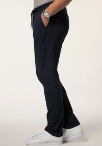 Navy Stretch-Jogginghosen mit einem elastischen Bund, Seitentaschen und schmalem Schnitt, kombiniert mit weißen Sneakers. Glatte Textur und schlichtes Design.