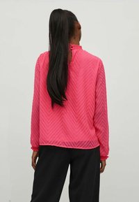 Pink chevron-patterned blouse with long sleeves and a ruffled neckline. Features a keyhole back detail and relaxed fit, paired with black pants.