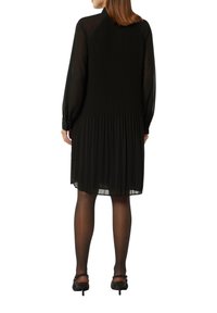 Robe noire plissée à manches longues, en tissu texturé, avec une silhouette légèrement évasée, présentant un col haut et des accents transparents au niveau des manches.
