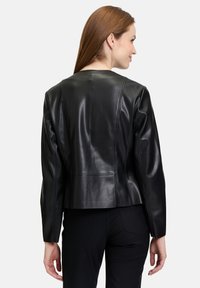 Veste en cuir noir avec un design ajusté, texture lisse et coutures détaillées. Présente un décolleté arrondi et une longueur cropped.