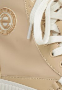 Beige hoge sneakers met een gladde synthetische bovenkant, witte veters en een cirkelvormig logo in een contrasterende kleur op de enkel.