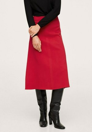 Red, knee-length skirt made of smooth fabric, with a fitted waist and straight silhouette. Paired with black, knee-high heeled boots.