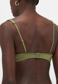 Grønn undertøystopp med smale stropper, sømløs band, justerbare detaljer, og en jevn tekstur, med et elegant og minimalistisk design.