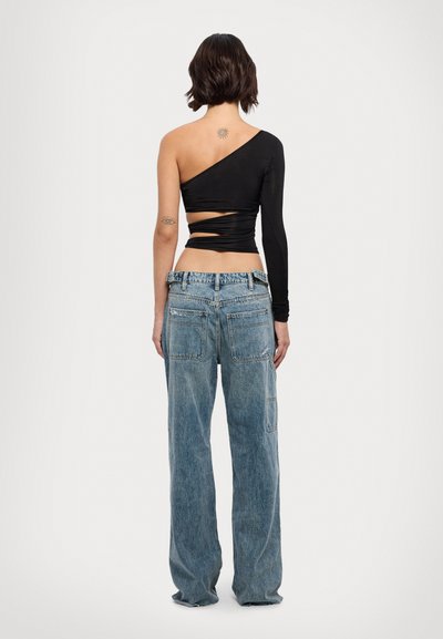Black asymmetrical long-sleeve top with a cutout detail at the waist, paired with loose-fitting light blue denim jeans.