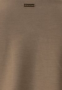 Brauner Stoff mit glatter Textur zeigt ein metallisches Logo-Tag. Das Design ist einfach und unverschönt, es konzentriert sich auf eine einfarbige Fläche.