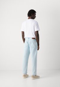 Light blue denim jeans with a relaxed fit, paired with a plain white t-shirt and beige sneakers. Features back pockets and brown leather tag.