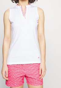 Vit ärmlös topp med dragkedjehals och rosa detaljer. Matchad med rosa shorts som har ett zickzackmönster i vita linjer.