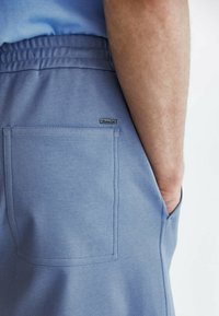 Shorts en coton bleu avec une ceinture élastique, une poche arrière avec un logo discret et des détails de couture apparents.