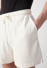 Fehér pamut rövidnadrág elasztikus derékkal és zsinórral. Oldalsó zsebekkel rendelkezik, puha tapintású. Lazány casual stílusú, egyenes szabású.
