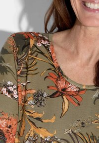 Bloemmotief top van olijfgroene stof, met levendige oranje en witte bloemen, ronde halslijn en een zachte, gestructureerde afwerking.