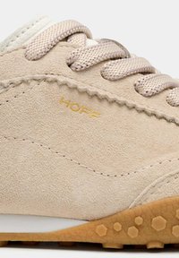 Baskets en daim beige avec lacets beiges, semelle en gomme à motif alvéolé, et logo "HOFF" doré sur le côté extérieur.