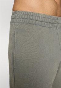 Calças jogger cinza claro feitas de tecido suave, com um cós elástico, bolsos laterais e uma textura lisa.