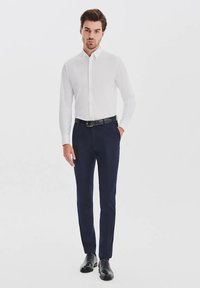 Biała koszula zapinana na guziki, ciemnogranatowe spodnie, czarny pasek i czarne buty. Slim fit, gładka tekstura materiału i klasyczny styl.