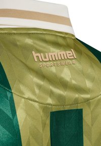 Grøn og gul sportsjersey med et geometrisk mønster, hvid krave og et guld "hummel SPORTSWEAR" logo. Glat tekstur.