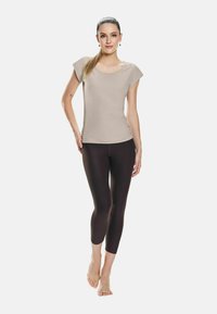 Top beige a maniche corte abbinato a leggings capri marrone scuro. Il top presenta un collo a vasca e un design aderente; i leggings hanno una texture liscia.