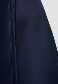 Tessuto blu navy con una superficie liscia, caratterizzato da cuciture visibili e un taglio pulito. Il design è aderente, enfatizzando una forma strutturata.