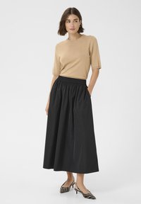 Top tricotat bej cu mâneci scurte, asociat cu o fustă neagră, cu talie înaltă și drapaj. Femeie care poartă pantofi cu imprimeu de zebră. Design simplu și elegant.