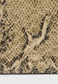 Kulta- ja musta keinonahkainen käärmeennahkamateriaali, jossa on teksturoitu, suomumainen kuvio; reunoilla on mustaa ommelta kestävyden parantamiseksi.