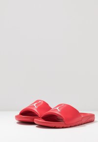 Infradito in gomma rossa con una parte superiore testurizzata e un logo in rilievo. La suola è piatta e presenta scanalature orizzontali per la trazione.