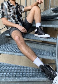 Košile s krátkým rukávem s abstraktním šedým a černým vzorem, kombinovaná s džínovými šortkami a černými kotníkovými teniskami s bílou podrážkou a logem.