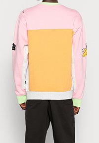 Sudadera colorida con una parte superior rosa, una sección media naranja y una parte inferior gris, con acentos en los puños verdes y detalles bordados en las mangas.