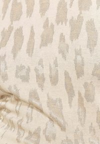 Beige tkanina s jemným vzorem leopardího tisku ve světle zlaté barvě, s texturovaným povrchem, který odráží světlo.