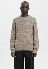 Beiger Strickpullover mit einer strukturierten Musterung, rundem Ausschnitt und gerippten Bündchen, kombiniert mit schwarzen Hosen. Einfaches und legeres Design.