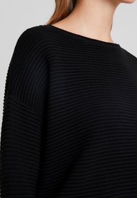 Svart ribbad tröja med bred halsringning och sänkta axlar, med strukturerad tyg och en luftig passform.